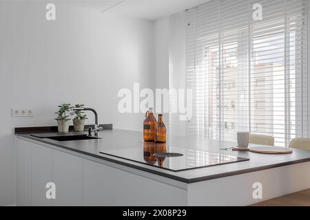 Une cuisine élégante et moderne avec un décor minimaliste avec des lignes épurées, un comptoir brillant et la lumière naturelle filtrant à travers des stores blancs Banque D'Images