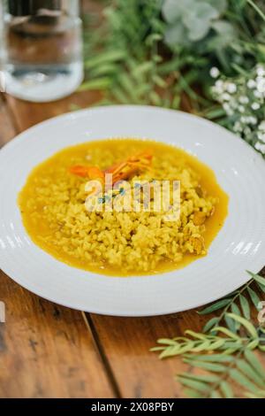 Une assiette vibrante de risotto aux crevettes, riche en couleurs et en saveurs, est assise de manière vivifiante sur une table en bois rustique avec un fond naturel et floral Banque D'Images