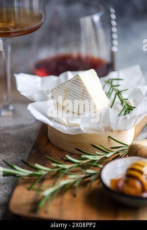 Un coin de fromage Brie sur une planche de bois, garni de romarin, accompagné de vin. Banque D'Images