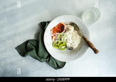 Vue de dessus sur un cadre de petit-déjeuner bien équilibré avec un bol blanc avec fromage cottage, yaourt naturel et graines de chia, accompagné de kiwi et de sicili Banque D'Images