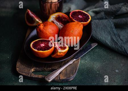 Oranges sanguines entières et tranchées affichées sur une assiette sombre avec un couteau vintage, sur un fond texturé vert foncé Banque D'Images