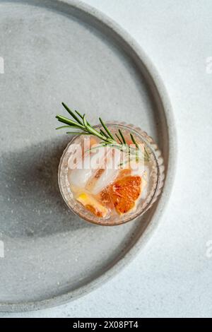 Vue de dessus d'un cocktail de vodka tonique confectionné orné de pamplemousse et de romarin, reposant sur un plateau texturé pour une expérience de service haut de gamme Banque D'Images