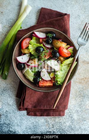 Vue de dessus d'une alléchante salade méditerranéenne élégamment présentée avec pommes de terre rôties aux herbes, tomates cerises juteuses, olives et radis croustillants Banque D'Images