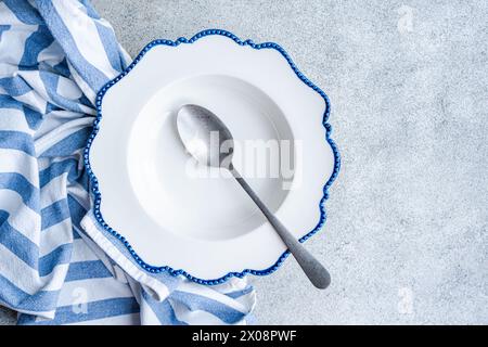 Élégante assiette à bords bleus avec une cuillère sur un tissu rayé sur une surface en pierre, mettant en valeur une configuration de salle à manger propre Banque D'Images