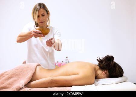 Masseuse appliquant de l'huile essentielle aromatique sur le dos d'un patient pour un massage thérapeutique dans un salon de spa Banque D'Images