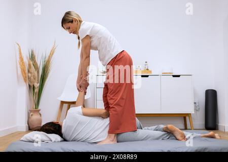 Un thérapeute effectuant un étirement manuel des jambes sur un patient dans une salle de physiothérapie calme et lumineuse Banque D'Images