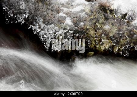 Une rivière gelée coule à travers un paysage montagneux, avec des glaçons suspendus à la corniche glacée au-dessus des courants rapides. Banque D'Images