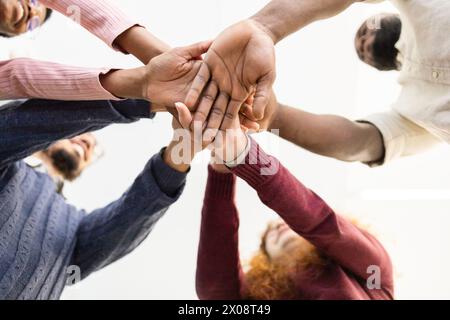 d'en bas, un groupe diversifié et méconnaissable de personnes empilent leurs mains dans une démonstration d'unité, de travail d'équipe et de collaboration. Ils examinent chacun d'eux Banque D'Images