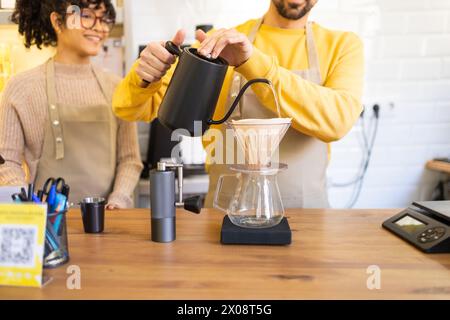 Le barista verse délicatement de l'eau chaude dans un goutteur de café au-dessus d'une carafe dans un cadre de café confortable. Banque D'Images