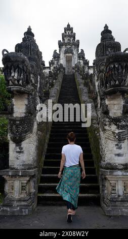 Vue arrière d'une voyageuse méconnaissable monte les anciens escaliers de Pura Penataran Agung Lempuyang, un célèbre temple balinais Banque D'Images