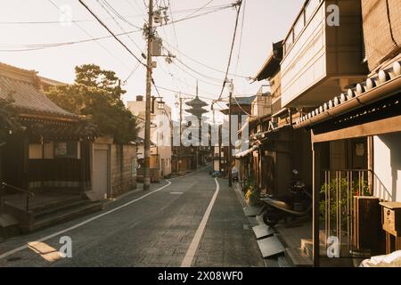 La lumière du soleil baigne une rue japonaise traditionnelle avec des maisons et une pagode en arrière-plan, capturant l'atmosphère calme Banque D'Images
