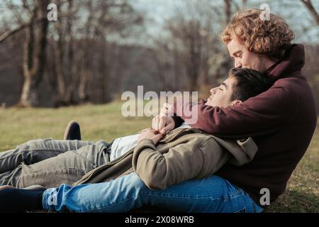 Un couple gay se détend dans les bras de l'autre, profitant d'un moment calme d'intimité et de confort sur un terrain herbeux mou sous le ciel ouvert Banque D'Images