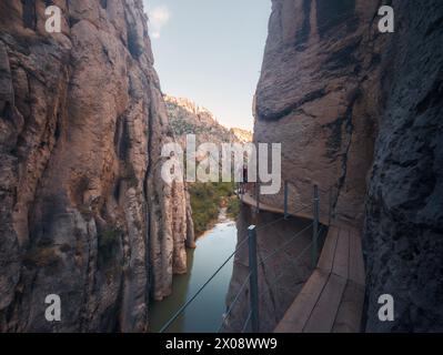 Un randonneur solitaire traverse une étroite promenade le long d'une falaise de montagne escarpée avec des eaux tranquilles en contrebas, incarnant l'esprit de voyage aventureux Banque D'Images