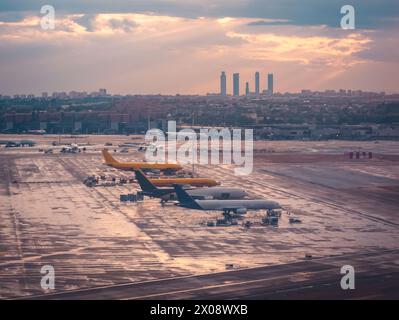 La piste de l'aéroport de Madrid profite de la lueur du coucher du soleil, avec des avions et l'horizon de la ville debout contre la lumière du soir Banque D'Images