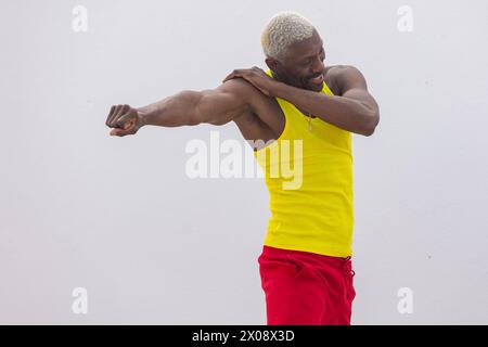 Un homme joyeux dans un débardeur jaune vif et un short rouge étire son bras, mettant en valeur un mode de vie sain et actif Banque D'Images