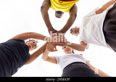 Sous un angle bas unique, les mains d'une équipe de basket-ball se rejoignent ci-dessus, symbolisant l'esprit d'équipe et les objectifs partagés avant le match Banque D'Images