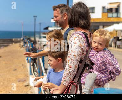 Une famille, avec une mère tenant un bébé garçon atteint du syndrome de Down, se tient aux côtés d'un père, d'une jeune fille et d'un garçon, tous engagés dans un moment partagé par le Banque D'Images