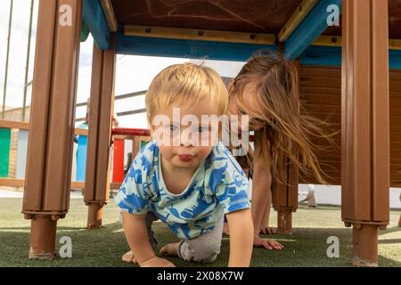 Une scène réconfortante avec un tout-petit atteint du syndrome de Down et une fille jouant sous une structure de terrain de jeu, mettant en valeur l'inclusivité et le lien familial dans un Banque D'Images