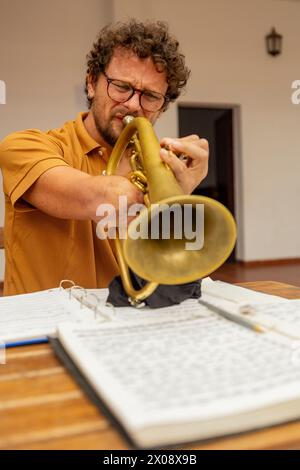 Un trompettiste masculin à un bras se plonge dans la musique, pratiquant sa trompette dans la tranquillité de sa cour intérieure. Banque D'Images