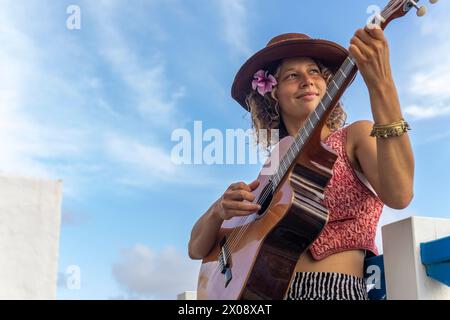 De dessous femme avec un chapeau et une fleur dans les cheveux joue de la guitare dans la rue, signifiant la passion pour la musique et la culture urbaine. Banque D'Images