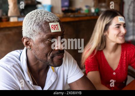 Les amis profitent d'un moment ludique dans un bar, s'engageant dans un jeu de devinettes amusant avec des mots sur leur front Banque D'Images