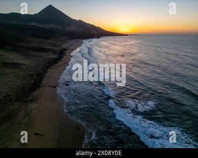 Une photo aérienne capture la beauté tranquille de la plage de Cofete, située contre les montagnes escarpées de la côte sud de Fuerteventura au coucher du soleil Banque D'Images