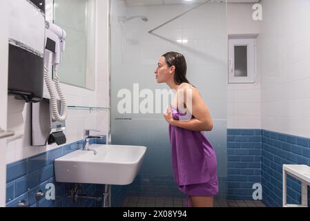 Femme enveloppée dans une serviette debout dans une salle de bain, se préparant à une douche Banque D'Images