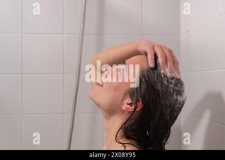 Une femme est capturée dans un moment de détente alors que l'eau coule sur elle, lavant le shampooing de ses cheveux pendant son temps de douche Banque D'Images