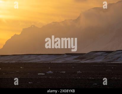 Coucher de soleil majestueux projetant des teintes dorées sur le paysage enneigé et les montagnes escarpées d'Islande Banque D'Images