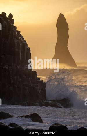 Un paysage marin islandais éthéré avec un empilement de mer imposant silhouette sur un ciel doré de coucher de soleil, tandis que les vagues s'écrasent sur les colonnes de basalte Banque D'Images