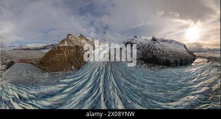 Une vue panoramique sur un glacier massif qui coule entre des montagnes escarpées sous un ciel islandais spectaculaire, soulignant la beauté gelée de la nature Banque D'Images