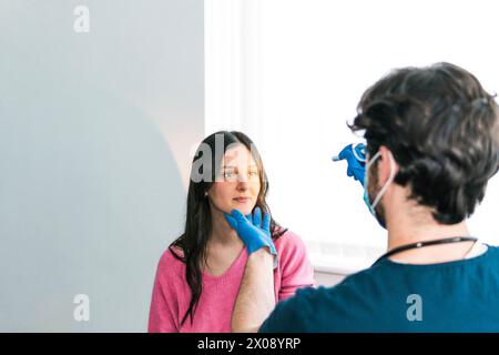 Un professionnel de la santé portant des gants palpe le cou d'un patient, vérifiant la présence de ganglions lymphatiques gonflés lors d'un examen de routine Banque D'Images