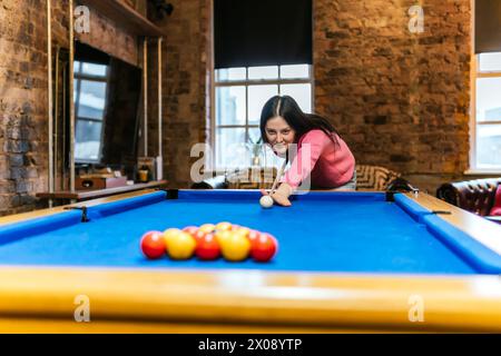 Une jeune femme avec une expression concentrée jouant au billard dans un cadre intérieur confortable, potentiellement avec des amis hors cadre Banque D'Images