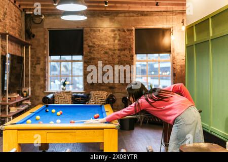 Deux jeunes amies profitent d'une partie ludique de billard dans une salle de jeux chaleureusement éclairée de style rustique avec une ambiance vintage Banque D'Images