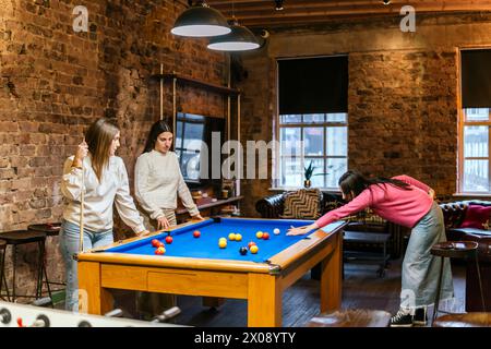 Les jeunes femmes amies apprécient un jeu décontracté de billard dans un intérieur confortable en briques Banque D'Images