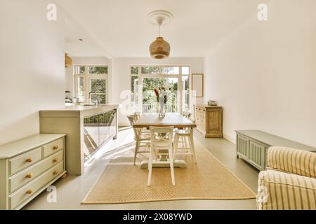 Coin cuisine spacieux et lumineux avec des luminaires contemporains, une table à manger et une vue panoramique sur le jardin à travers de grandes fenêtres. Banque D'Images