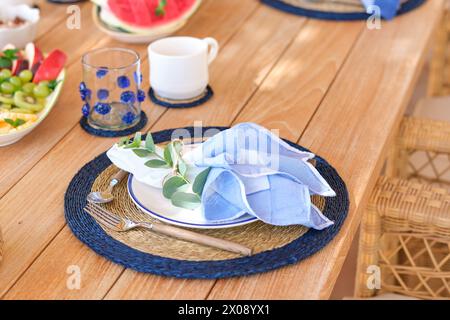 Une vue rapprochée d'une table de petit déjeuner sur une terrasse, mettant en valeur une élégante assiette et couverts avec une touche de verdure Banque D'Images