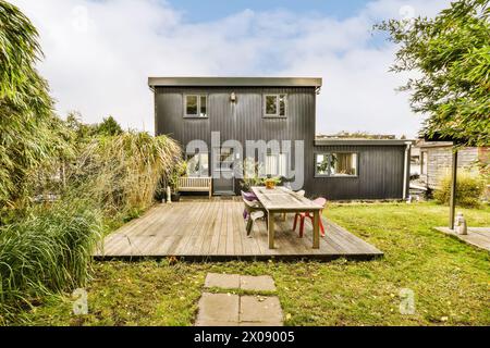 Une charmante maison de banlieue de deux étages avec une terrasse en bois et une salle à manger extérieure entourée d'une végétation luxuriante. Banque D'Images