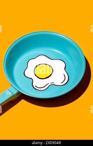 Une image vibrante montrant un dessin simpliste d'un œuf frit centré dans une poêle turquoise brillante sur un fond jaune. Banque D'Images