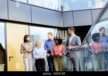 Groupe de collègues dans un caucus d'affaires décontracté, partageant des idées à côté d'une façade en verre réfléchissant à la fin de la journée. Banque D'Images