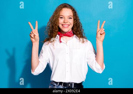 Photo de magnifique jolie fille joyeuse porter des bras de vêtements blancs élégants montrant le symbole v-sign isolé sur fond de couleur bleue Banque D'Images