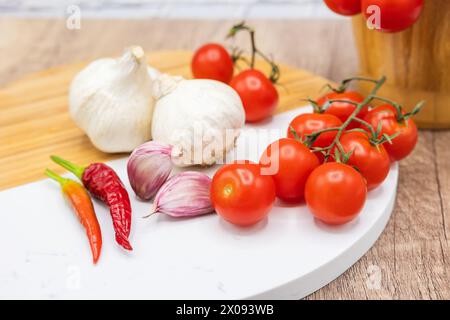 ingrédients dans la cuisine, tomates cerises de vigne avec de l'ail et du poivre frais sur une planche de bois et du mortier pour hacher Banque D'Images