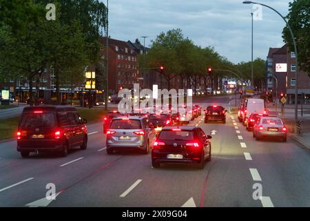 Hambourg, Allemagne - 19 mai 2023 : les véhicules s'alignent à un feu de circulation dans une rue de la ville pendant le crépuscule, avec la lueur des feux arrière rouges et la lâche de rue Banque D'Images