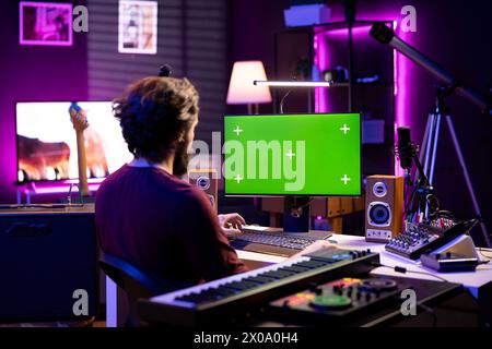 Ingénieur du son apprenant à mixer et à maîtriser des enregistrements audio en regardant des didacticiels de post-production en ligne sur pc avec l'écran vert. L'artiste édite des morceaux et règle le volume dans le home studio. Banque D'Images