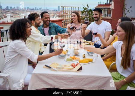 Groupe de jeunes heureux grillant du vin rouge et célébrant le repas sur le toit Banque D'Images