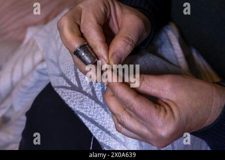 Vue rapprochée des mains de la femme dans le processus de couture. Tissu à coudre à la main avec aiguille sur le lieu de travail. Mains de couturière tenant le tissu pour la fabrication Banque D'Images