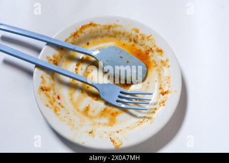 Assiette vide sale, fourchette et couteau sur assiette blanche. Couverts usagés, symbolisant la fin du déjeuner ou du dîner. Banque D'Images