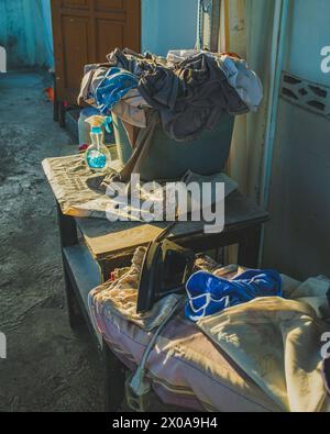 un panier à linge débordant de vêtements colorés se trouve sur une table en bois brun clair. Un fer bleu et un vaporisateur blanc se trouvent à droite du BA Banque D'Images