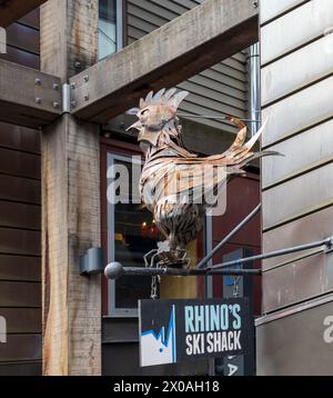 Queenstown, Nouvelle-Zélande- 3 avril 2024 : confectionnée avec des plumes détaillées, une sculpture de coq en métal monte la garde au-dessus du panneau pour Rhinos ski Shack, A. Banque D'Images