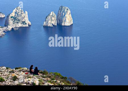 2 personnes assises au sommet de la falaise surplombant les rochers Faraglioni, Piccola, Capri, Campanie, Italie, Europe Banque D'Images